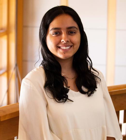 Aditi Jain smiling with face and torso in frame standing inside Dutton Hall with window in the background