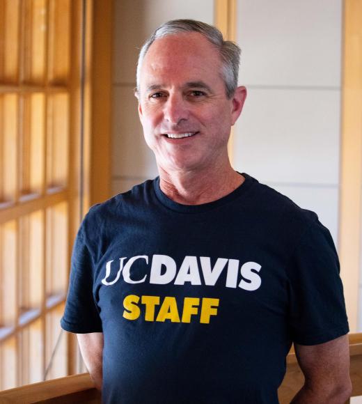 Grant Acosta smiling with face and torso in frame standing inside Dutton Hall with window in the background