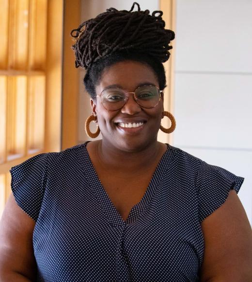 Inez Anders smiling with face and torso in frame standing inside Dutton Hall with window in the background