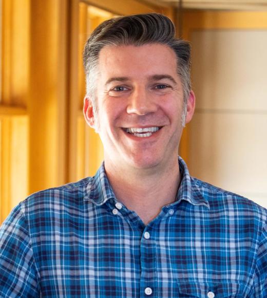James Parmenter smiling with face and torso in frame standing inside Dutton Hall with window in the background