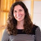 Ariel Loring smiling with face and torso in frame standing inside Dutton Hall with window in the background