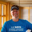 Duff Harrold in a baseball cap smiling with face and torso in frame standing inside Dutton Hall with window in the background