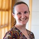 Jennifer Healey smiling with face and torso in frame standing inside Dutton Hall with window in the background