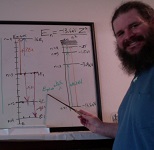 Casey Davis, Math and Physics Specialist in AATC smiling and pointing at a diagram on a whiteboard.